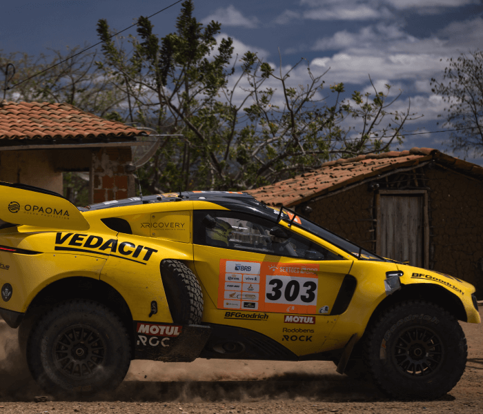 Carro esportivo amarelo. Ao fundo, uma casa.