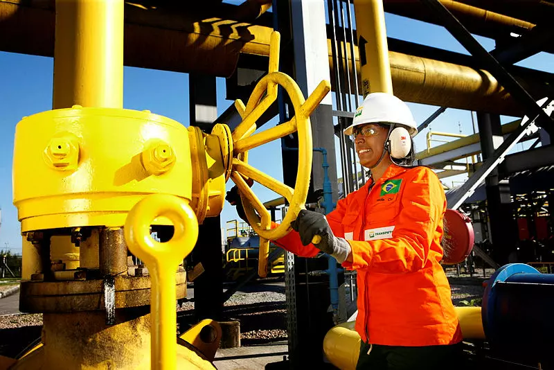 Mulher em uniforme laranja girando uma válvula de metal.